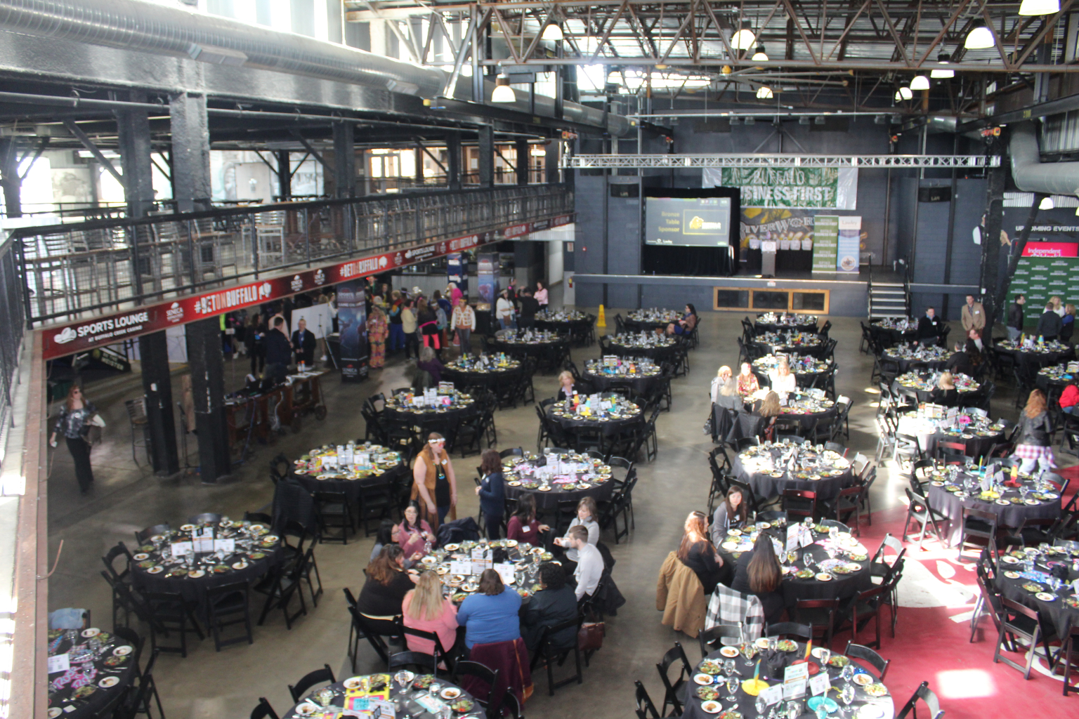 Hundreds of guests at round tables across the full RiverWorks floor beneath the mezzanine