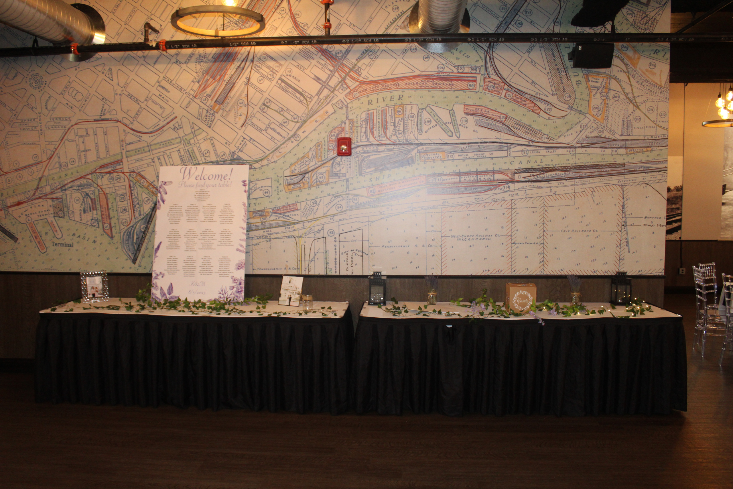 Long skirted table dressed with greenery and lanterns against the rail map mural