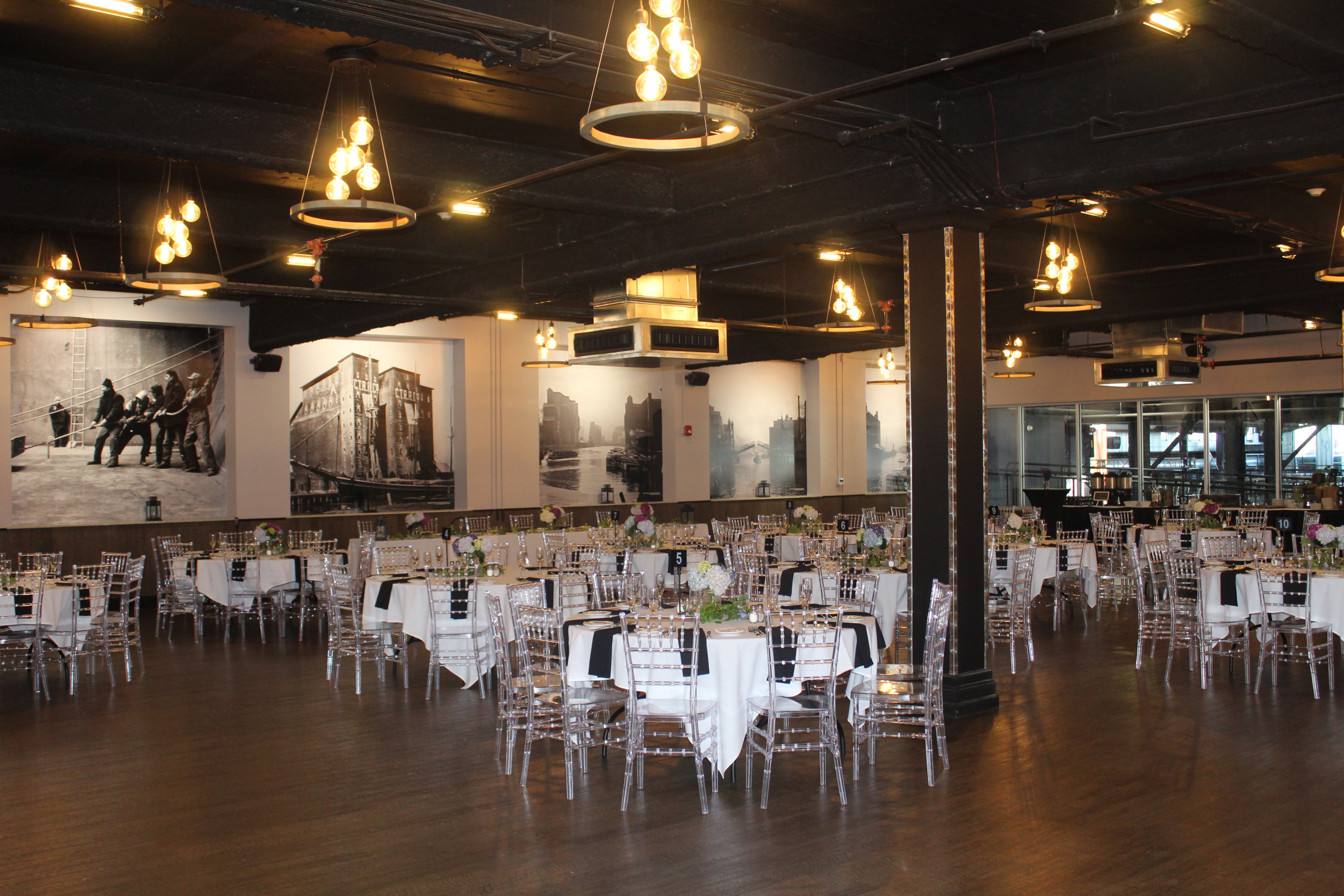 Round tables and clear chiavari chairs filling the Silos Event Center under the pendant rings