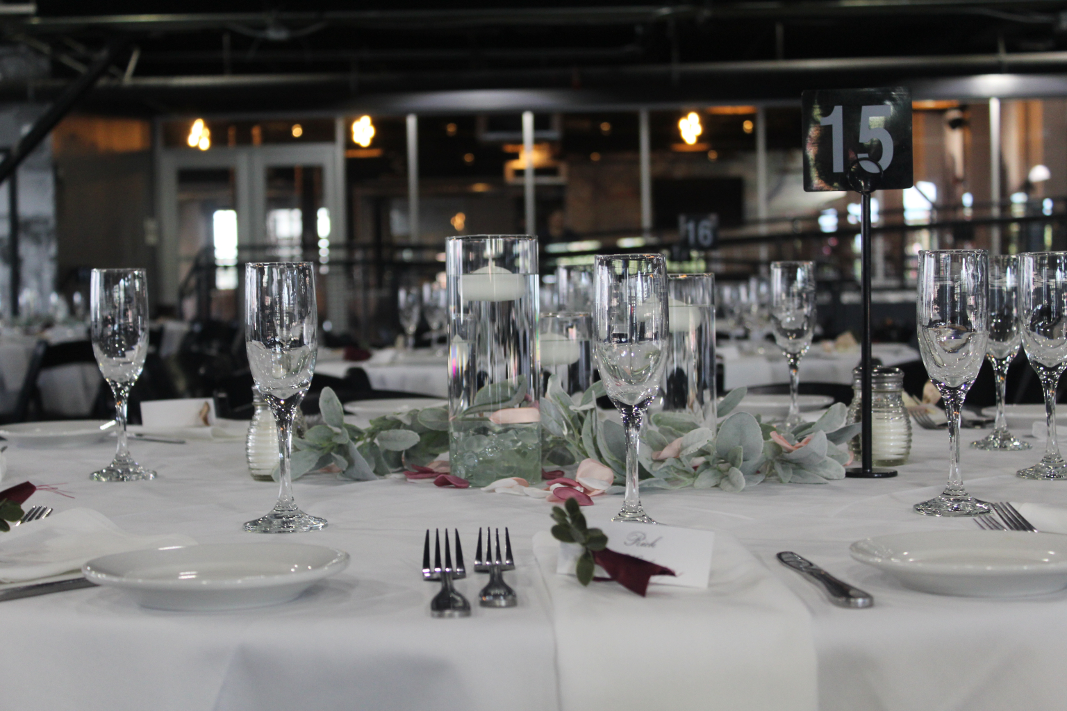 Close view of a place setting with stemware, greenery and a table number
