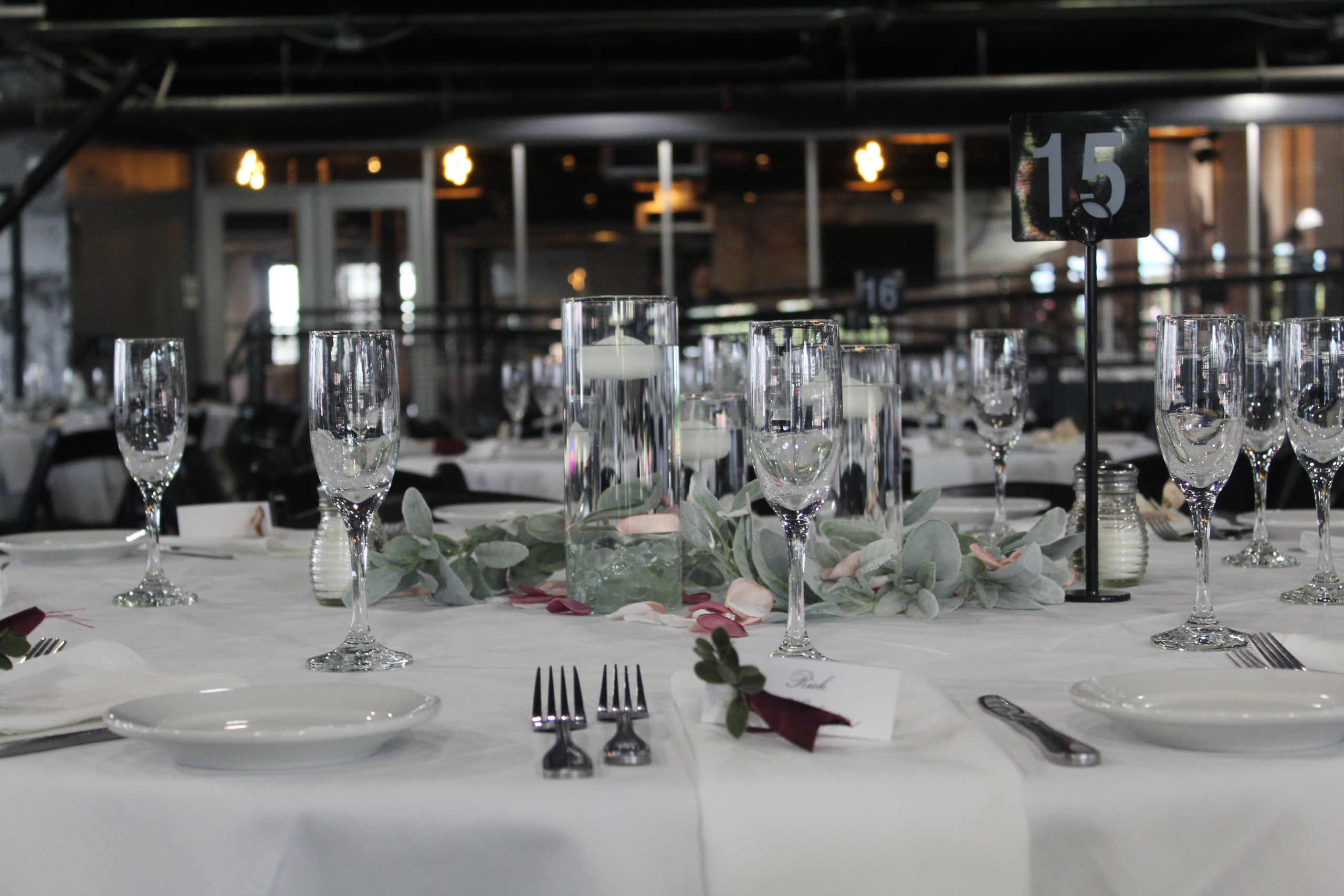 Close view of a place setting with stemware, greenery and a table number