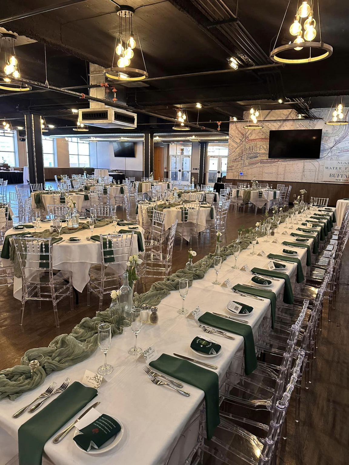 Long banquet table set with white linen, green napkins and glassware under the pendant lights