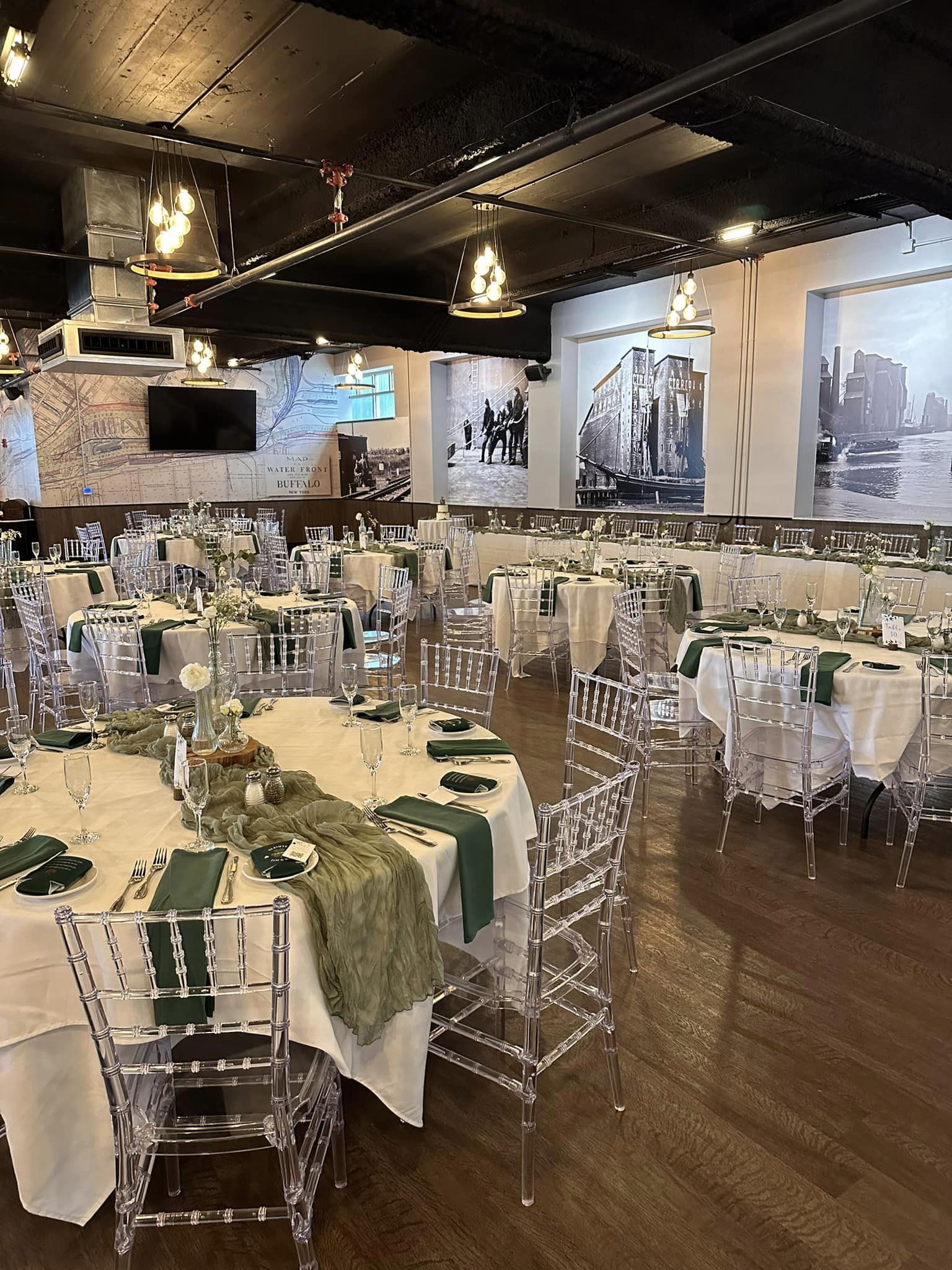 Long banquet table set with green runners, glassware and clear chiavari chairs