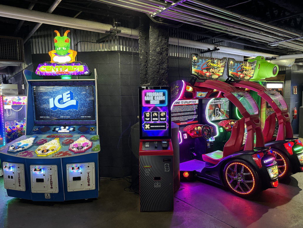 Arcade games and a ride-on racing game lit up on the RiverWorks arcade floor