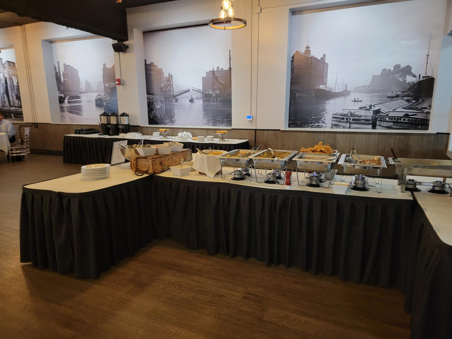 Buffet line set with chafing dishes, serving pans and stacked plates along a black skirted table