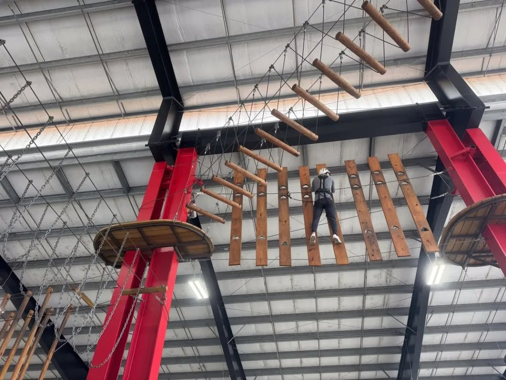 A climber crossing a wooden plank bridge on the ropes course