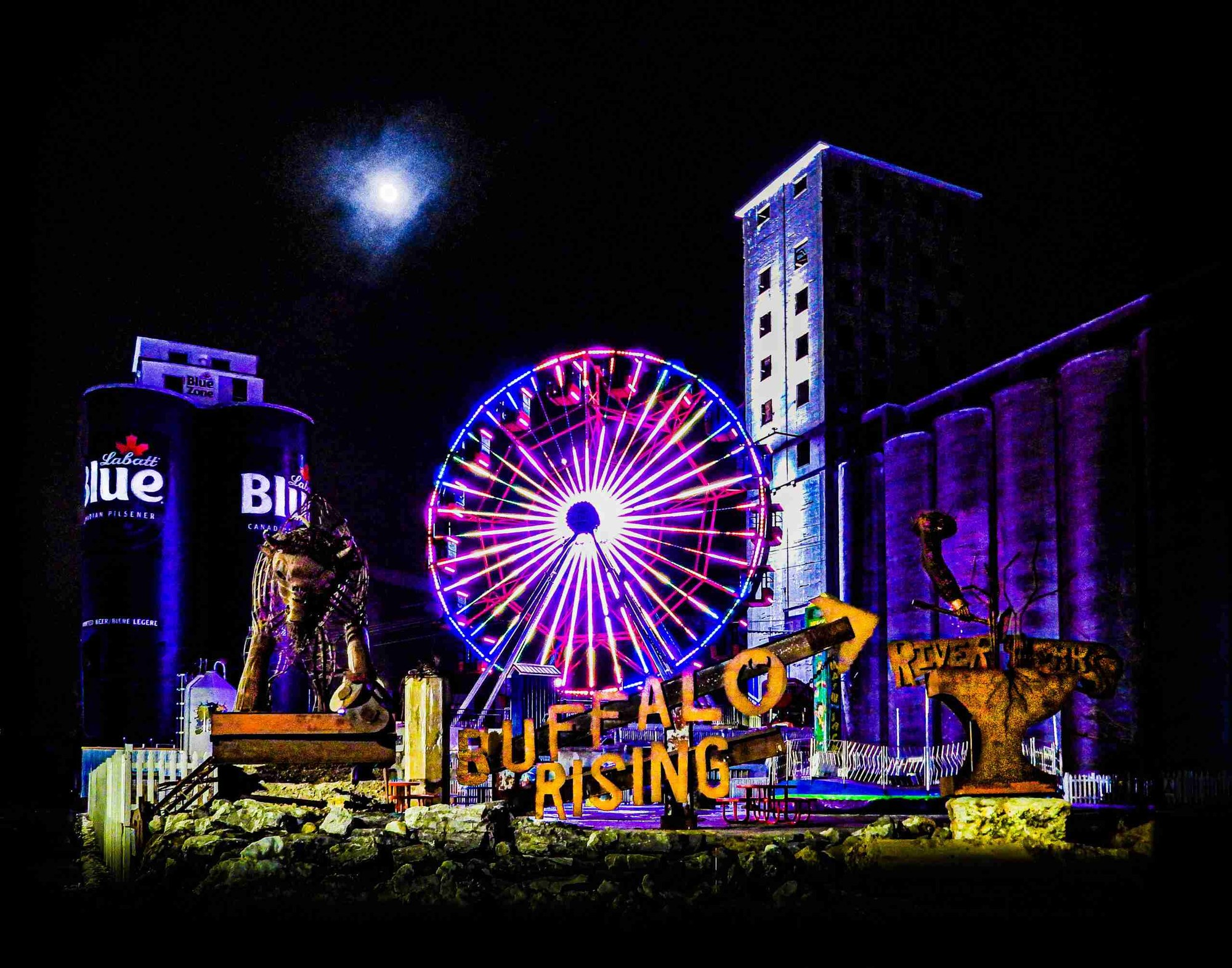 The Buffalo Rising sign, grain silos and ferris wheel lit at night